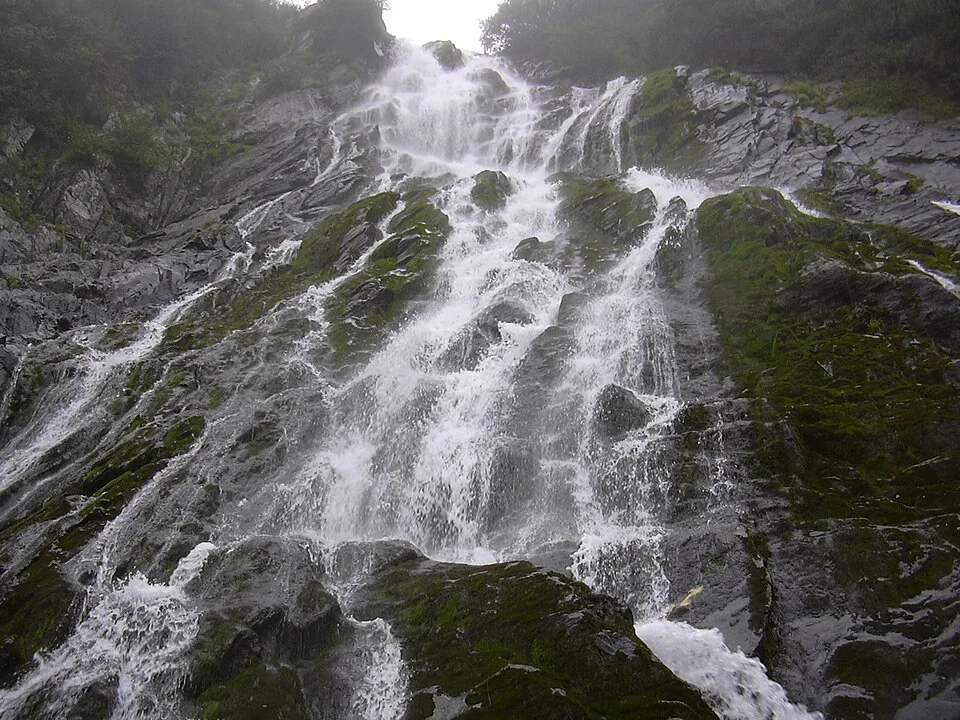 Looking straight up the Bâlea Waterfall's stepped cascade as sheets of white water crash down dark, moss-covered rock in a wall of spray.