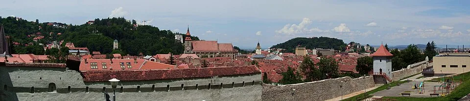 A wide panorama of Brașov's old town rooftops, church spires and towers, seen looking down from the slopes of Tâmpa.